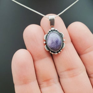 May include: A silver chain necklace with a pendant featuring a purple oval gemstone set in a silver bezel with a decorative border.