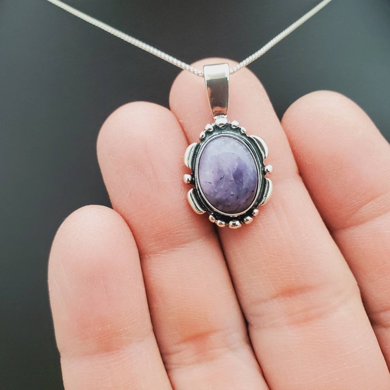 May include: A silver chain necklace with a pendant featuring a purple oval gemstone set in a silver bezel with a decorative border.