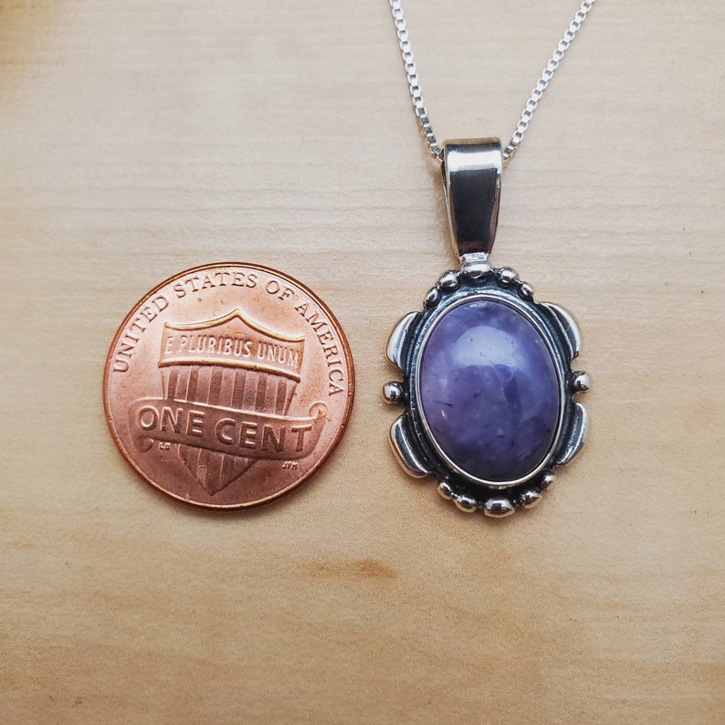 May include: A silver pendant necklace with a purple gemstone set in a silver oval frame. The pendant is about the size of a US penny.