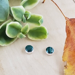 May include: A pair of silver stud earrings with green malachite stones. The earrings are small and round, and the malachite has a swirling pattern.
