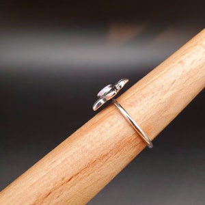 May include: A silver ring with a pink opal flower design. The ring is on a wooden display stand.
