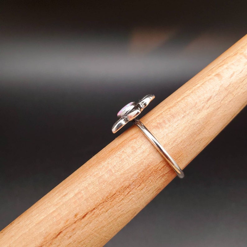 May include: A silver ring with a pink opal flower design. The ring is on a wooden display stand.