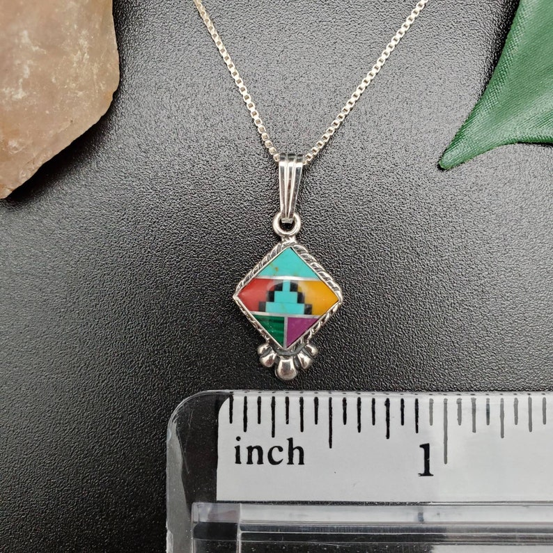May include: A silver necklace with a square pendant featuring a geometric design of turquoise, red, yellow, green, and purple stones. The pendant is about 3/4 inch wide.
