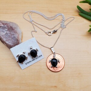 May include: Sterling silver necklace and earrings set featuring black onyx turtle pendants. The necklace is on a silver chain and the earrings are stud style. The set is displayed on a wooden surface with a penny for size reference.