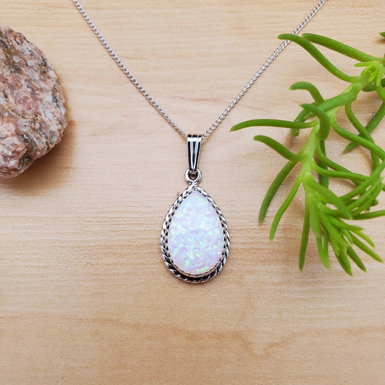 May include: A silver chain necklace with a teardrop-shaped pendant featuring a white opal stone with a silver border.