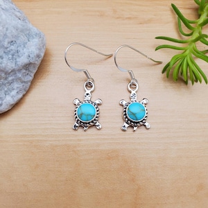 Puede incluir: Un par de pendientes de plata con forma de tortuga con piedras turquesa. Los pendientes son de estilo colgante con cierre de gancho.