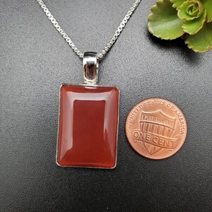 May include: A silver chain necklace with a pendant featuring a rectangular carnelian gemstone. The pendant is about the size of a US penny.