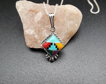 May include: A silver chain necklace with a diamond-shaped pendant featuring a turquoise, red, yellow, green, and purple inlay.