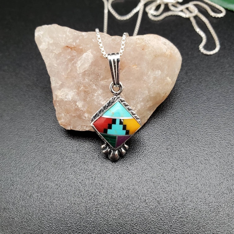 May include: A silver chain necklace with a diamond-shaped pendant featuring a turquoise, red, yellow, green, and purple inlay.