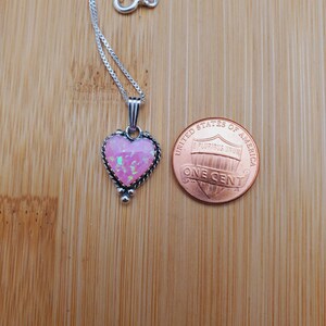 May include: A silver heart-shaped pendant necklace with a pink opal stone. The pendant is about the size of a US penny.