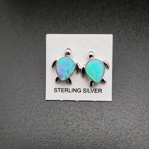 Könnte beinhalten: Ein Paar Ohrringe aus Sterlingsilber mit einem blauen Opal-Schildkröten-Design. Die Ohrringe befinden sich auf einer weißen Karte mit dem Aufdruck "Sterling Silver".