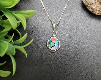 May include: A silver chain necklace with a small oval pendant featuring a geometric design of turquoise, coral, and black stones.