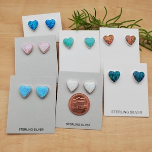 May include: Six pairs of sterling silver heart earrings with different colored opal stones. The earrings are displayed on white cards with the words "Sterling Silver" printed on them.