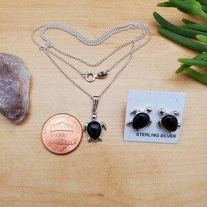 May include: Sterling silver necklace and earrings set featuring black onyx turtle pendants. The necklace has a delicate chain and the earrings are stud style.