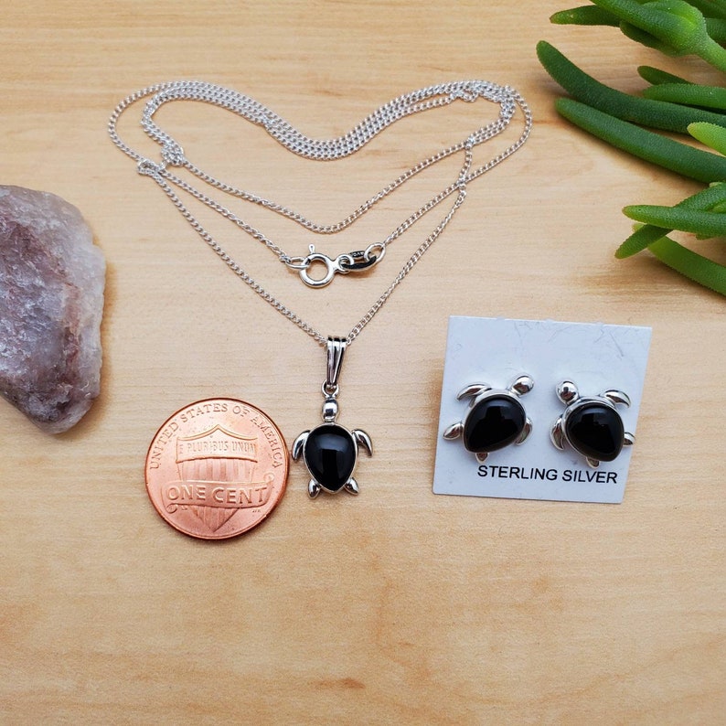 May include: Sterling silver necklace and earrings set featuring black onyx turtle pendants. The necklace has a delicate chain and the earrings are stud style.