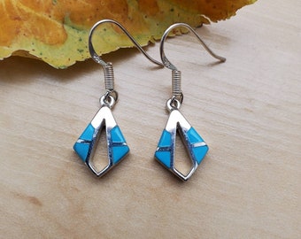 May include: A pair of silver dangle earrings with turquoise inlay in a geometric pattern. The earrings have a diamond shape with a silver wire design.