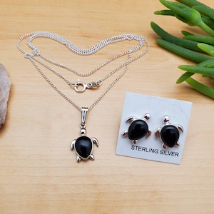 May include: Sterling silver necklace and earrings set featuring black onyx turtle pendants. The necklace has a delicate chain and the earrings are stud style.