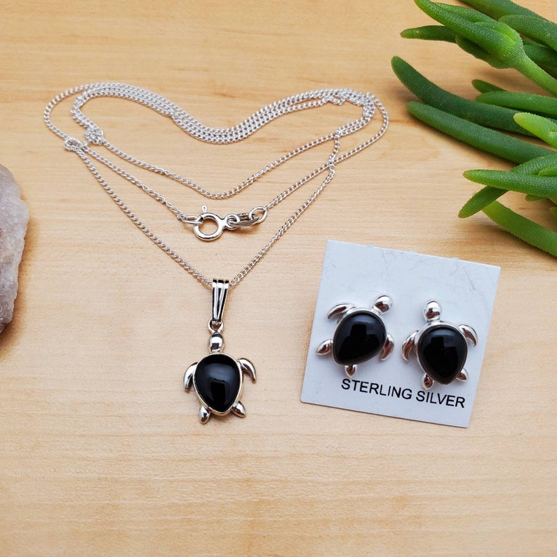 May include: Sterling silver necklace and earrings set featuring black onyx turtle pendants. The necklace has a delicate chain and the earrings are stud style.