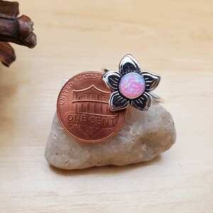 May include: A silver ring with a pink opal flower design. The ring is shown next to a US penny for size comparison.