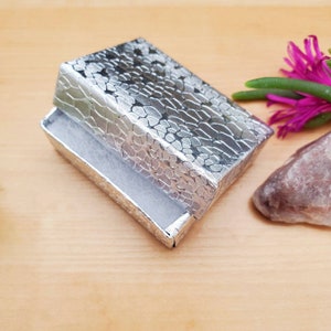 May include: A silver gift box with a textured pattern, open and lined with white tissue paper.
