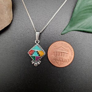 May include: A silver chain necklace with a pendant featuring a geometric design inlaid with turquoise, red, yellow, and green stones. The pendant is about the size of a US penny.