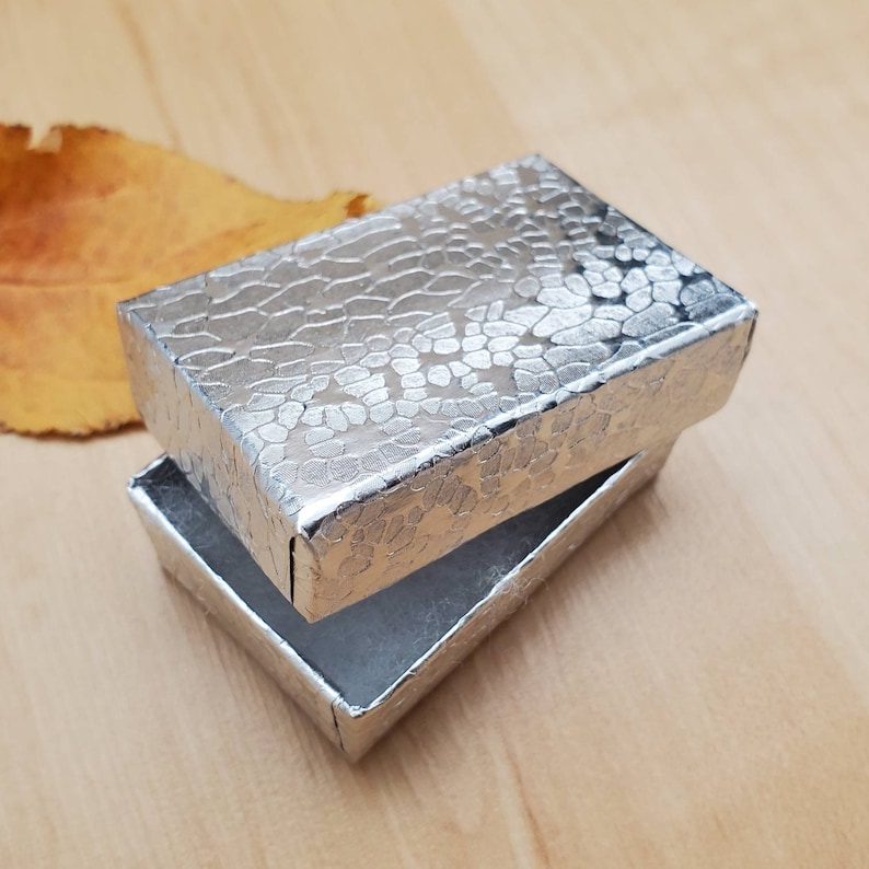 May include: A silver gift box with a textured pattern. The box is open and the inside is lined with white paper.