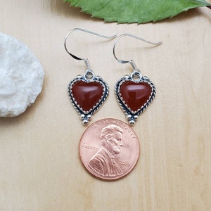 May include: A pair of sterling silver heart-shaped earrings with carnelian stones. The earrings are about the size of a US penny.