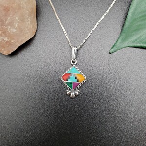 May include: A silver necklace with a square pendant featuring a geometric design of turquoise, red, green, and yellow stones.