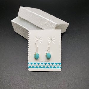May include: A pair of sterling silver earrings with turquoise stones. The earrings are displayed on a white card with the text "Sterling Silver".