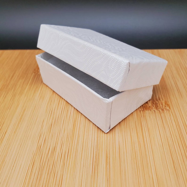 May include: A white cardboard box with a textured lid. The lid is open and the box is empty.