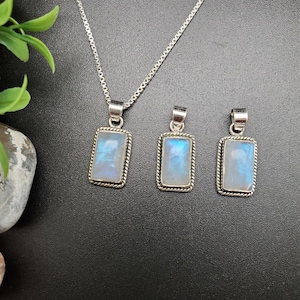 May include: Three silver pendants with rectangular moonstone stones. The pendants are on a black background. The largest pendant is on a silver chain.