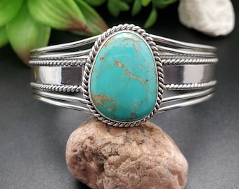 May include: A silver cuff bracelet with a turquoise stone set in a rope design. The stone is a light blue color with brown veins.