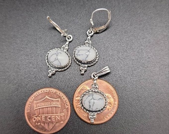 May include: A set of silver earrings and a pendant featuring white and gray marbled stones. The jewelry is displayed on a black surface with a penny for scale.