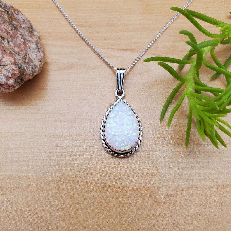 May include: A silver chain necklace with a teardrop-shaped white opal pendant. The pendant has a silver rope-like border.