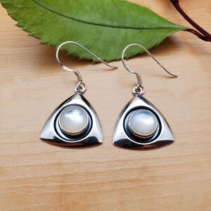 May include: A pair of silver earrings with a white mother of pearl stone set in a triangular frame.