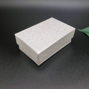 May include: A white gift box with a textured, wavy pattern. The box is closed and has a smooth, flat surface.