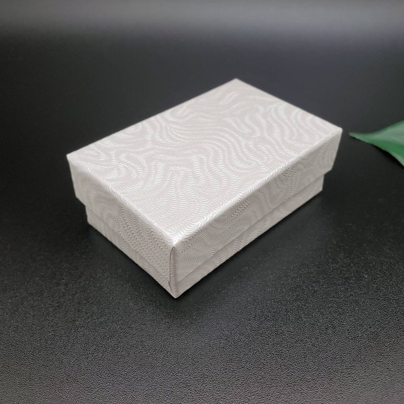 May include: A white gift box with a textured, wavy pattern. The box is closed and has a smooth, flat surface.
