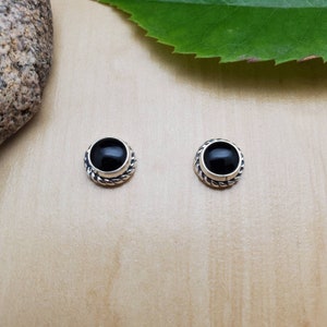 May include: A pair of silver stud earrings with black onyx stones. The stones are set in a twisted silver bezel.