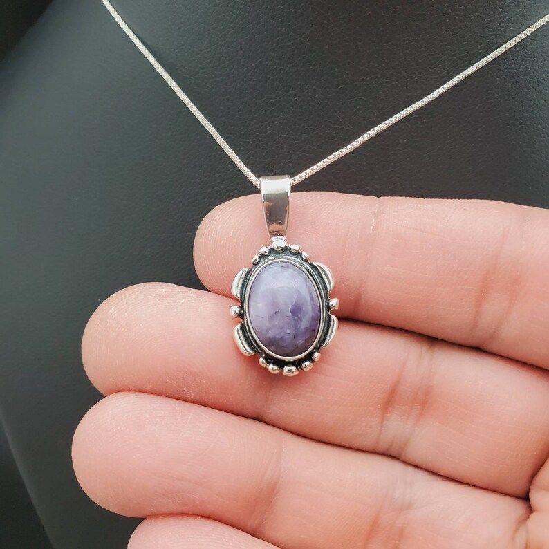 May include: A silver chain necklace with a pendant featuring a purple oval gemstone set in a silver frame with a detailed design.