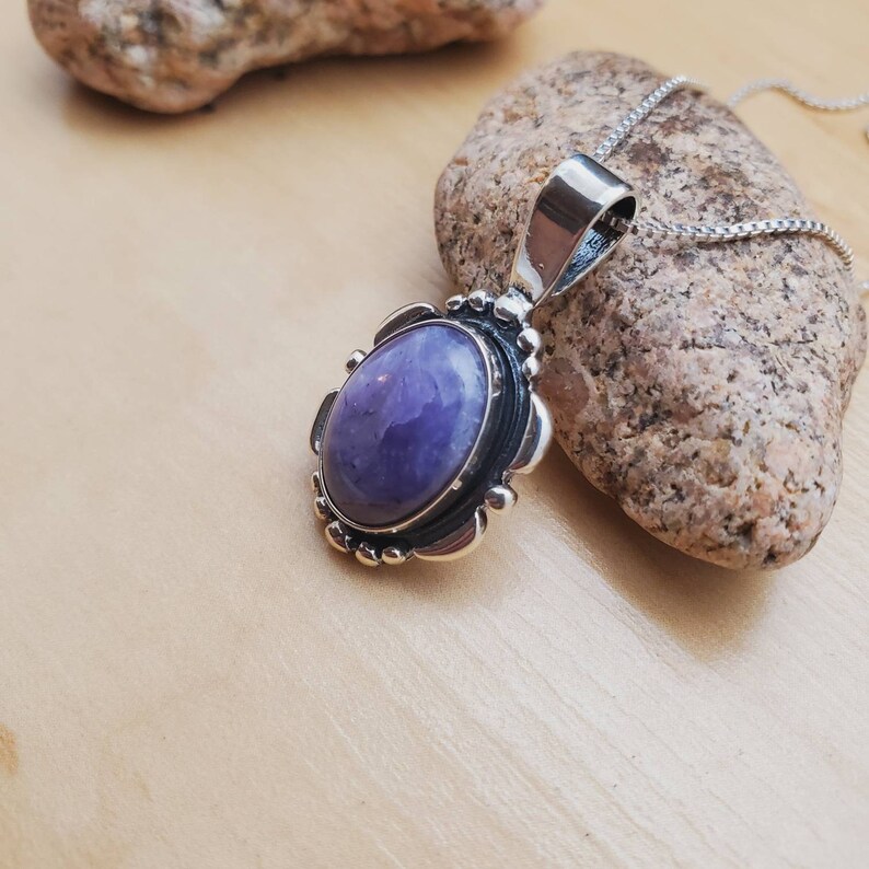 May include: A silver pendant with a purple amethyst stone set in a detailed silver frame. The pendant is on a silver chain.