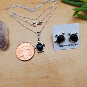 May include: Sterling silver turtle necklace and earrings set with black onyx stones. The pendant and earrings are both in the shape of a turtle. The necklace is on a silver chain. The earrings are on a card that says "Sterling Silver".