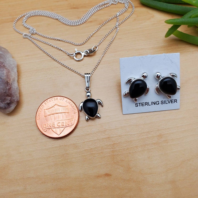 May include: Sterling silver turtle necklace and earrings set with black onyx stones. The pendant and earrings are both in the shape of a turtle. The necklace is on a silver chain. The earrings are on a card that says "Sterling Silver".