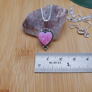 May include: A silver heart-shaped pendant necklace with a pink opal stone. The pendant is approximately 1 inch in length. The necklace is on a silver chain.