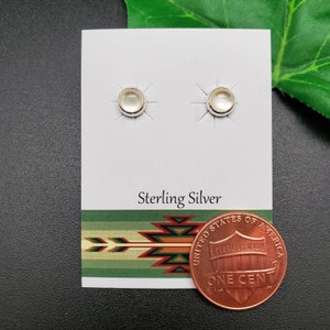 May include: A pair of sterling silver earrings with white round stones. The earrings are displayed on a white card with the words "Sterling Silver" printed on it. A penny is included for size reference.