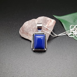 May include: A silver pendant necklace with a dark blue rectangular gemstone set in a silver frame.