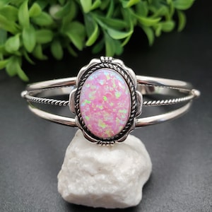 May include: A silver bracelet with a pink opal stone set in a silver bezel. The bracelet has a twisted wire design.