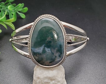 May include: A silver bracelet featuring a green agate stone set in a silver bezel. The bracelet has a twisted rope design on the band.