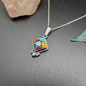 May include: A silver necklace with a geometric pendant featuring a colorful inlay of turquoise, red, green, purple, black, and yellow stones.