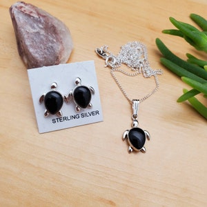 May include: Sterling silver turtle necklace and earrings set with black onyx stones. The necklace has a delicate chain and a pendant featuring a turtle with a black onyx stone in the center. The earrings are stud earrings with a turtle design and black onyx stones.