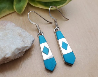 May include: A pair of dangle earrings with a turquoise and silver design. The earrings are shaped like a teardrop and have a silver diamond in the center.